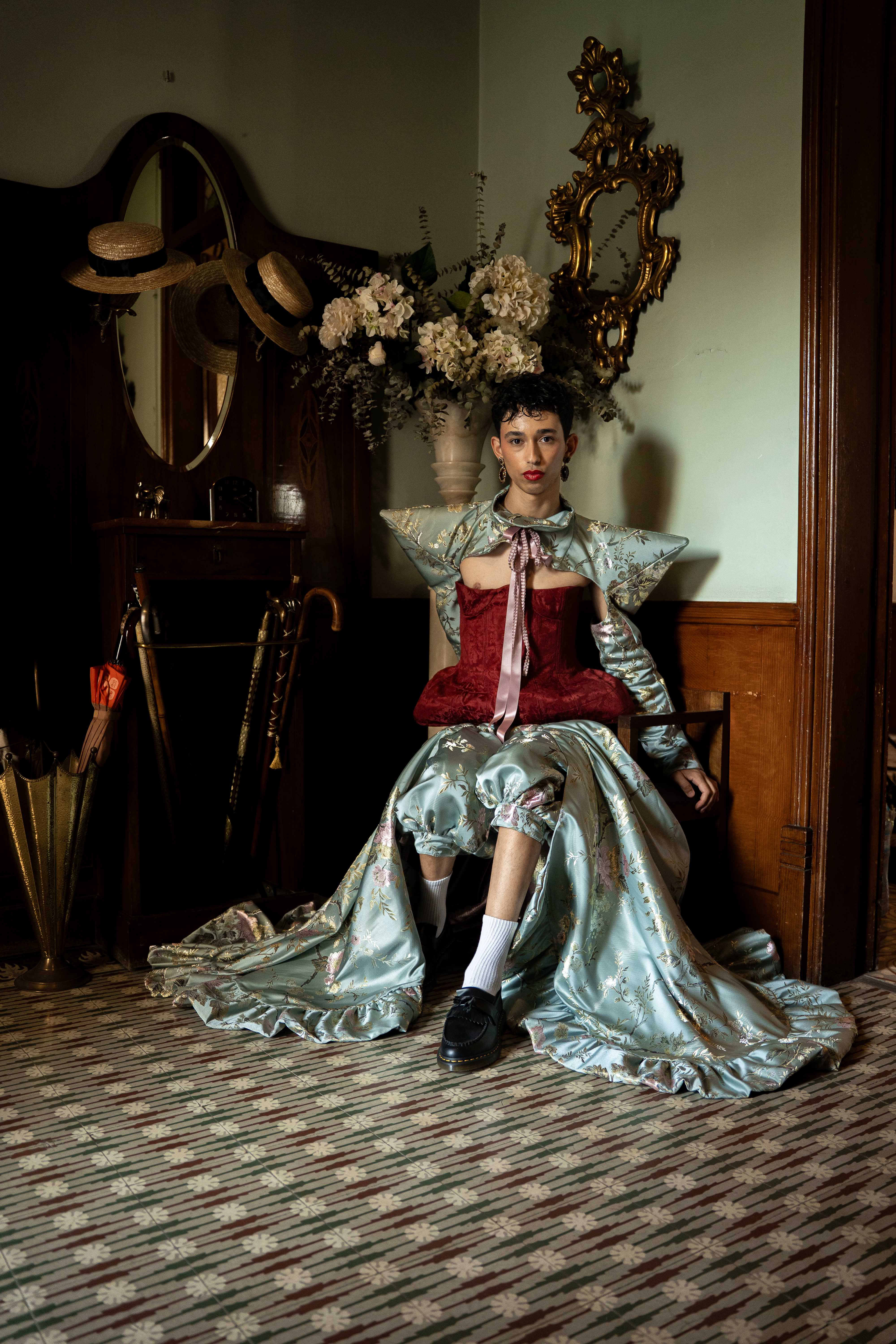 Mona Puppet Riot FW25 — seated model with star collar and brocade gown, theatrical knitwear Barcelona