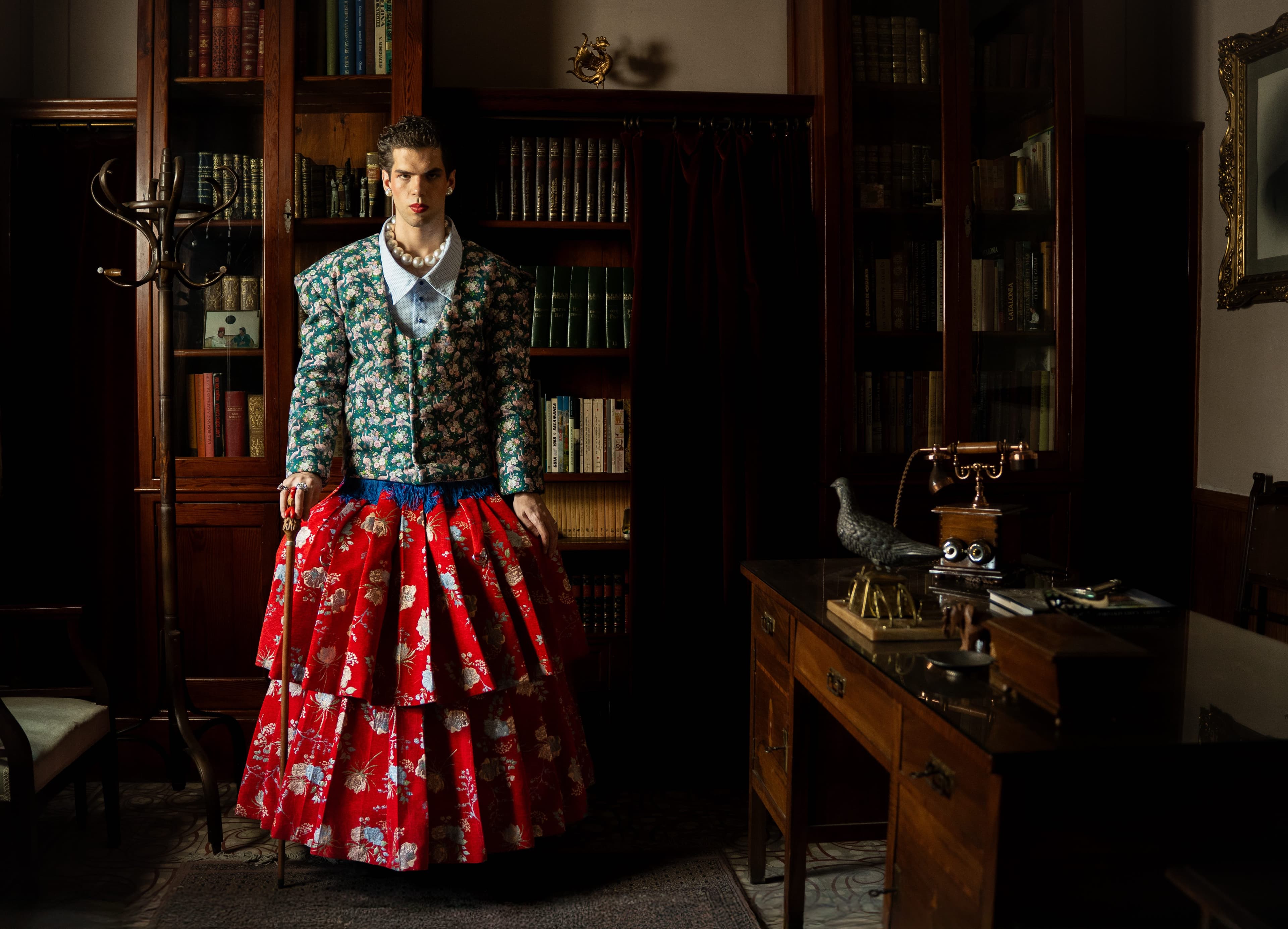 Mona Puppet Riot FW25 — editorial scene with floral jacket and red tiered brocade skirt, Barcelona fashion designer